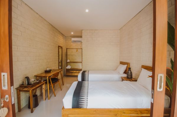 Cozy Balinese-style twin bedroom with wooden beds, beige brick walls, and tropical accents.